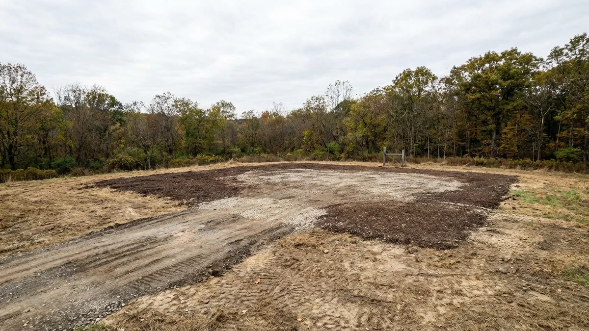 Cleared rural lot in Warren County New Jersey prepared for pole barn construction with mulched ground, gravel access road, and surrounding wooded property